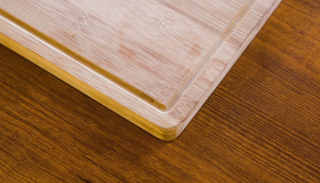 Close-up of the corner of a natural bamboo cutting board with a juice groove on a wooden table.
