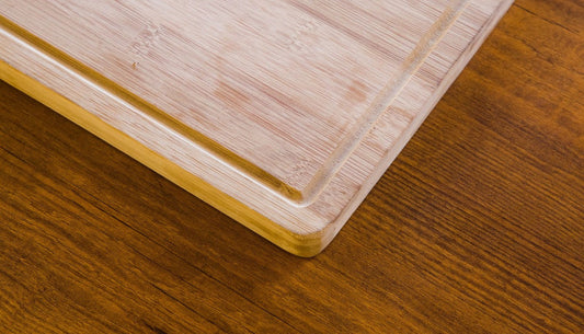 Close-up of the corner of a natural bamboo cutting board with a juice groove on a wooden table.