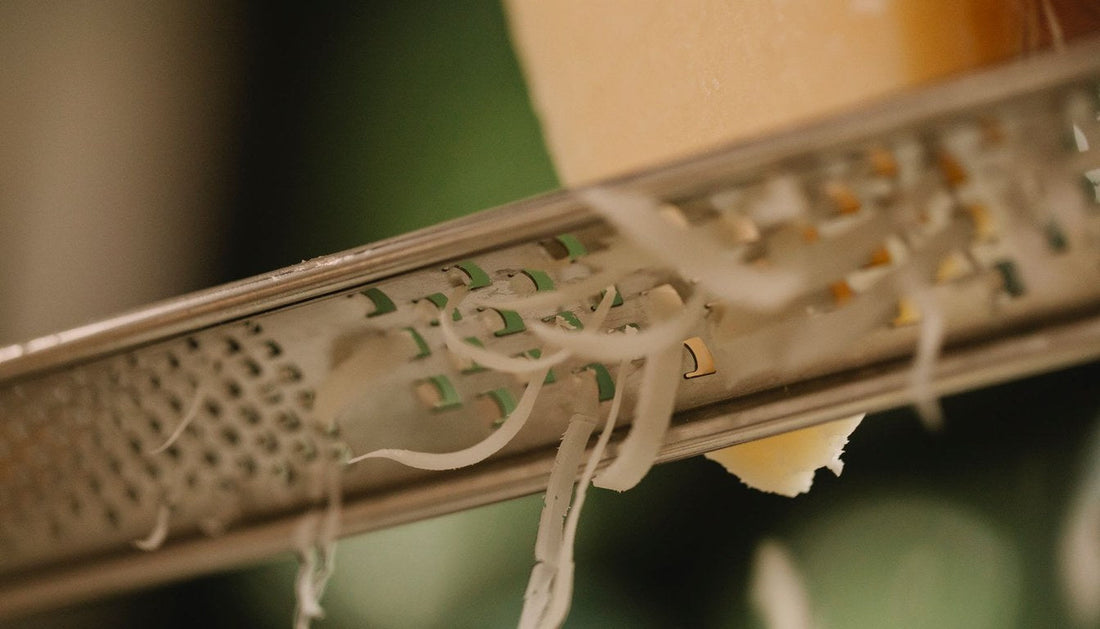 Close-up of hard cheese being grated on a narrow stainless steel rasp grater.
