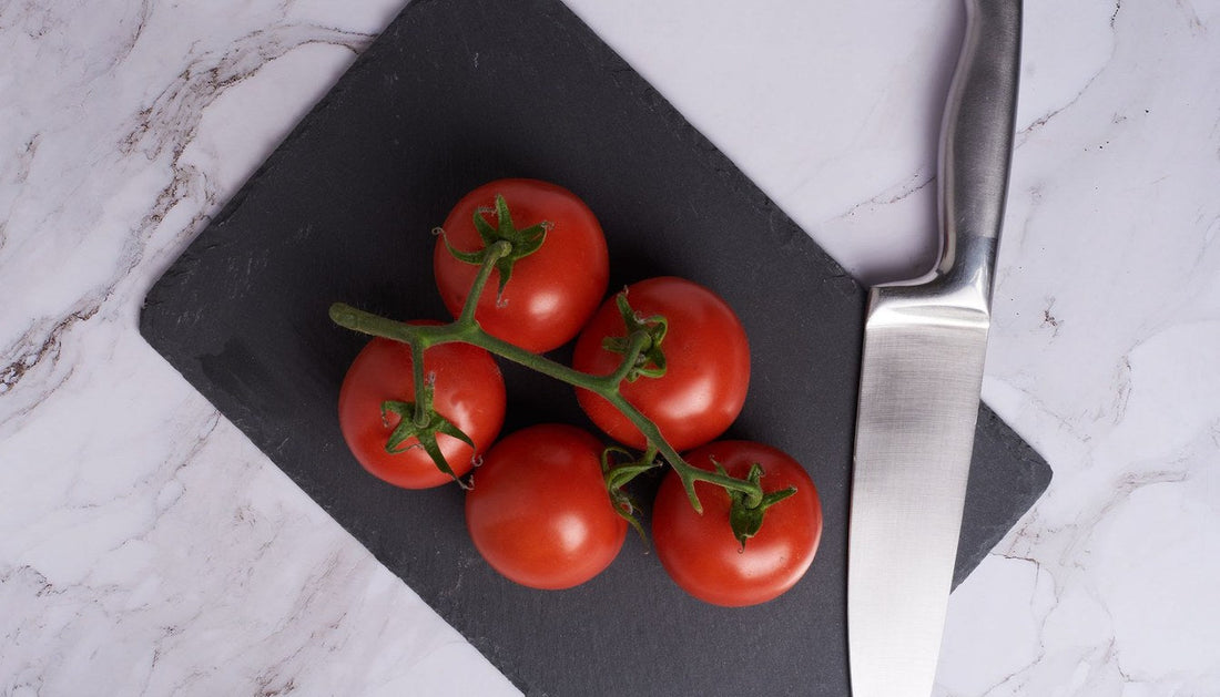 Vine tomatoes and a chef's knife on a black slate board on a marble counter.