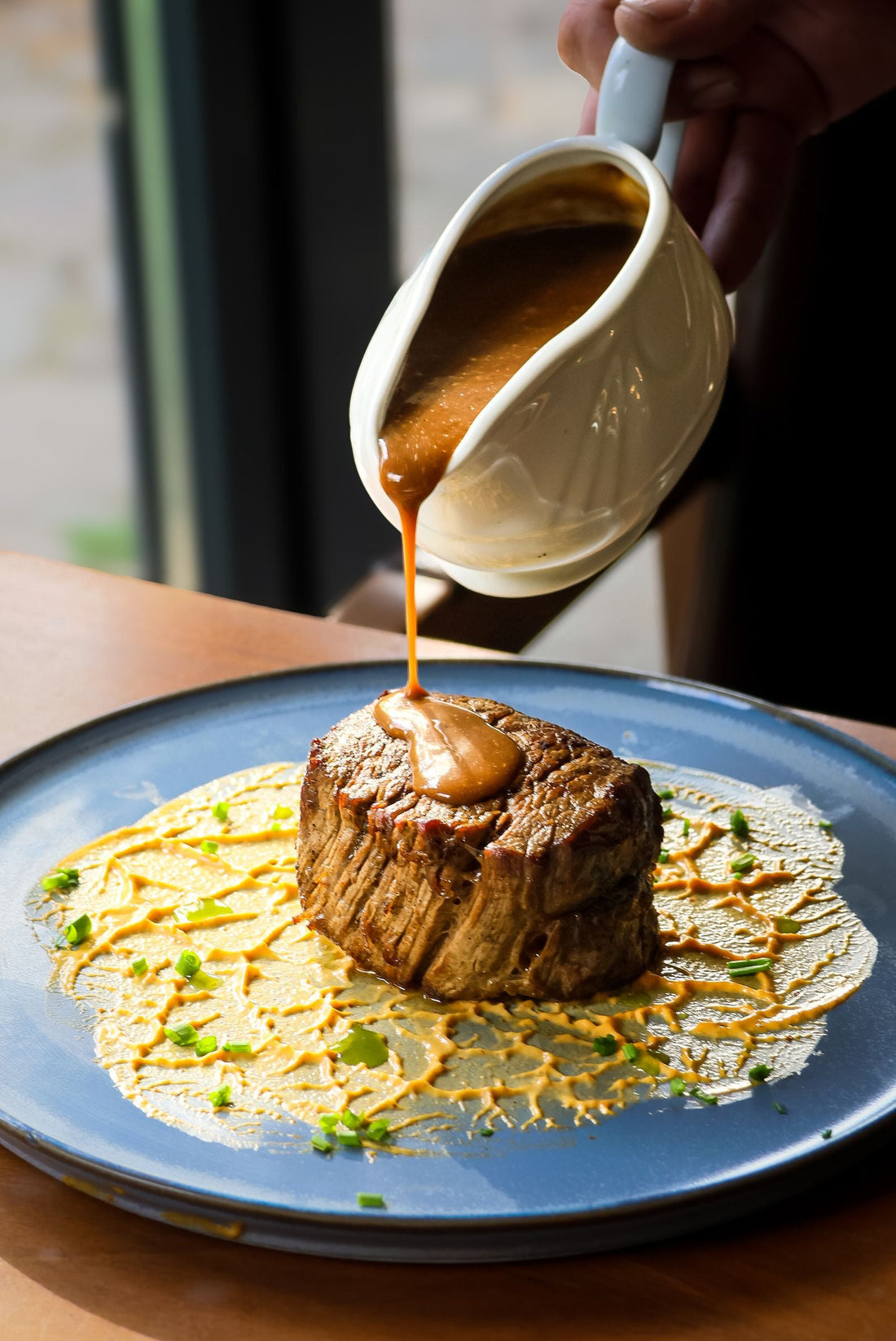 Gravy being poured from a gravy boat over a plated steak.