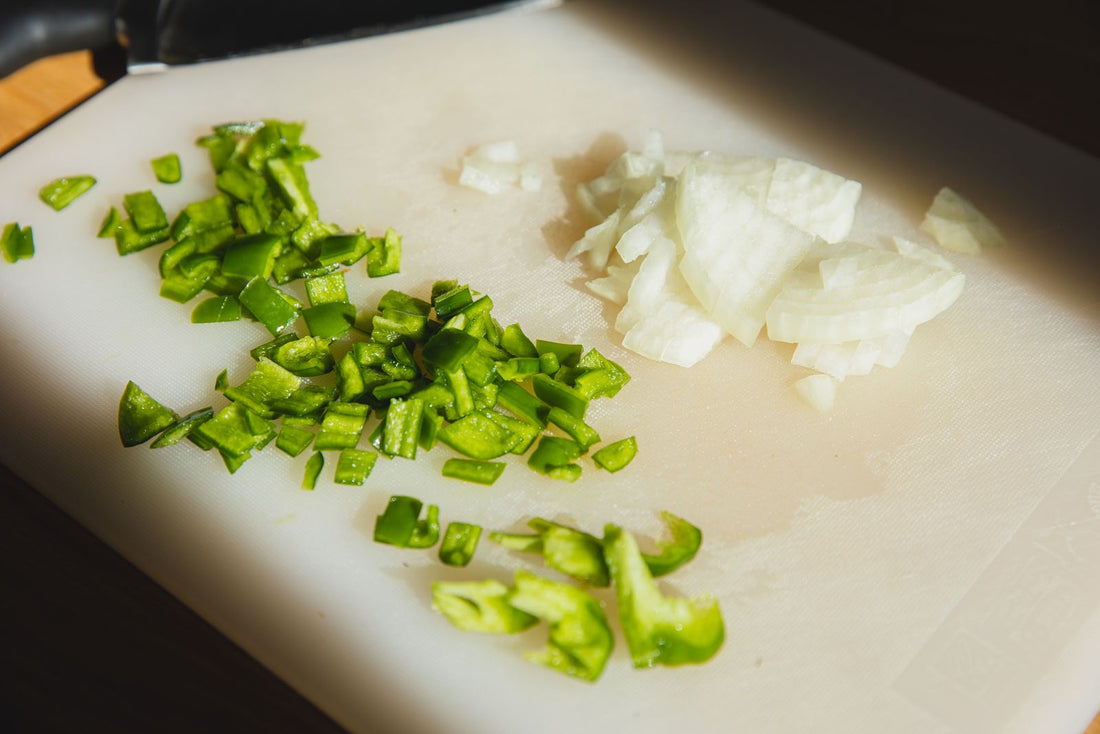 Chopped green pepper and onion on a white cutting board.