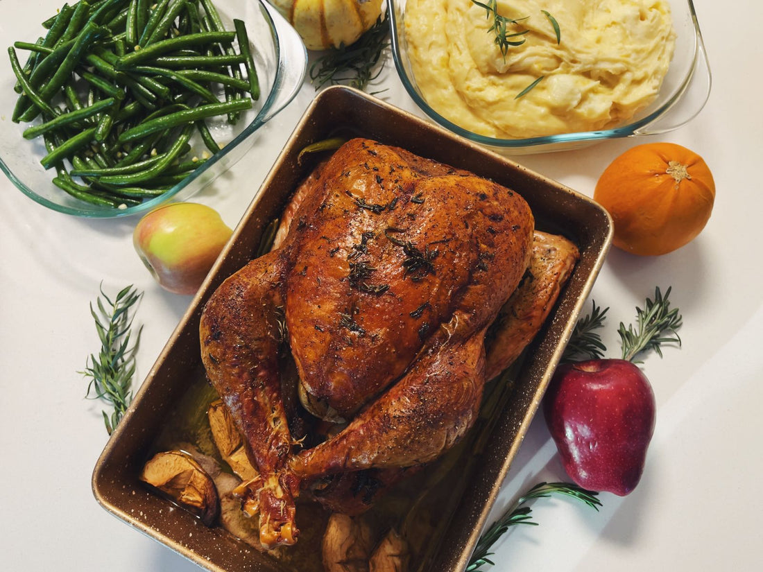 A roast turkey in a dark roasting pan surrounded by green beans, mashed potatoes, and fruit.