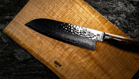 A santoku knife with a hammered, patterned blade resting on a wooden cutting board.