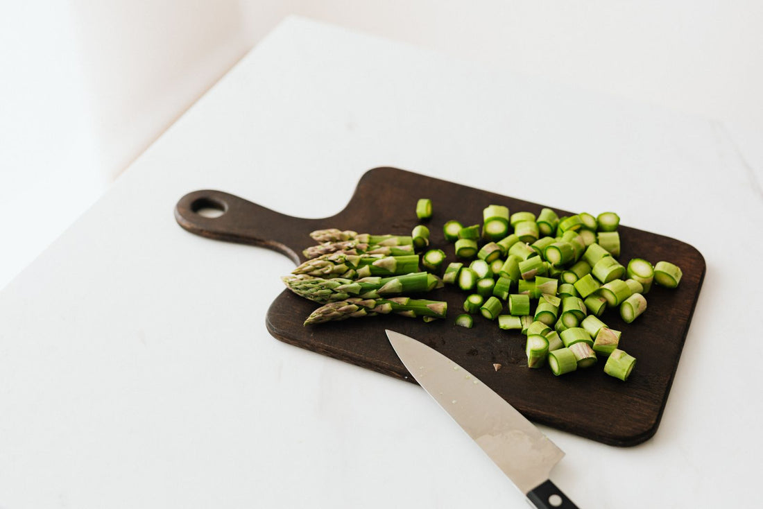 Chopped asparagus and a chef knife on a thin dark cutting board with a handle.