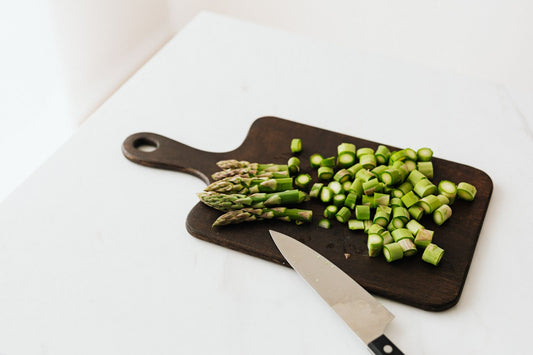 Chopped asparagus and a chef knife on a thin dark cutting board with a handle.