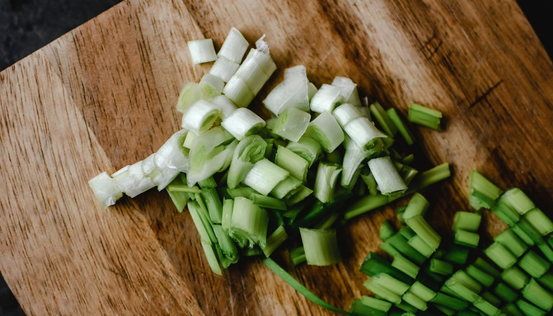 Chopped green onions on a wooden cutting board, white ends and green tops in separate piles.