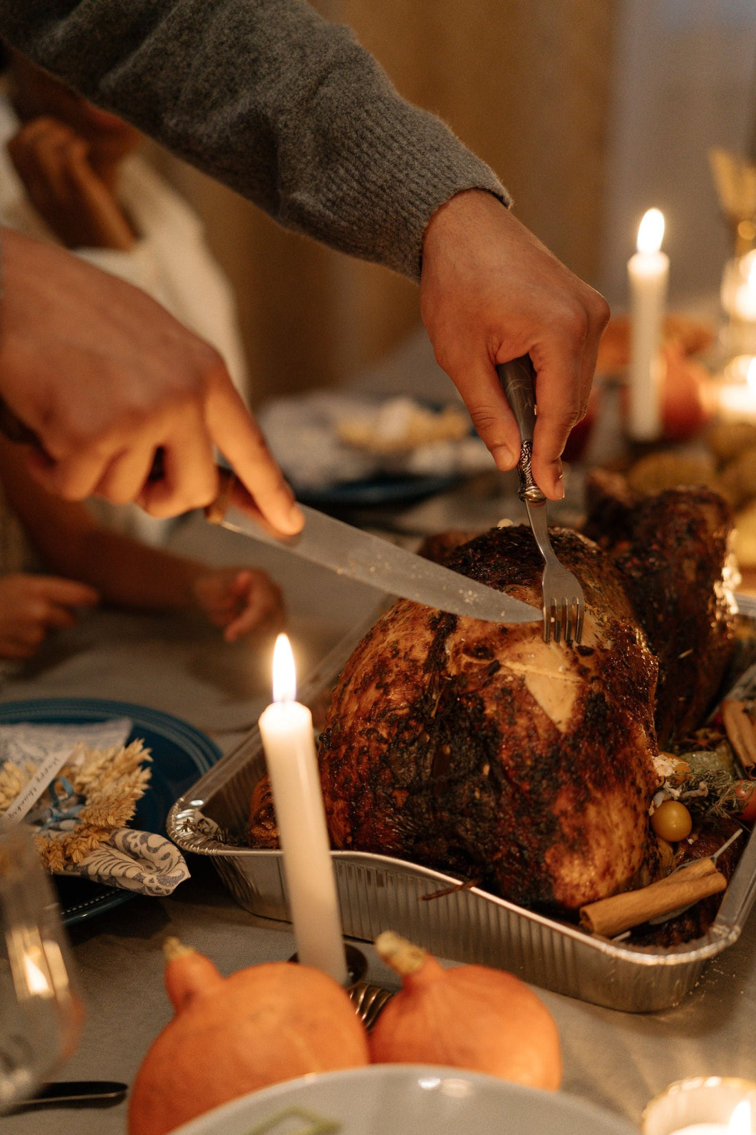 A host carving a roast turkey in a pan at a holiday table.