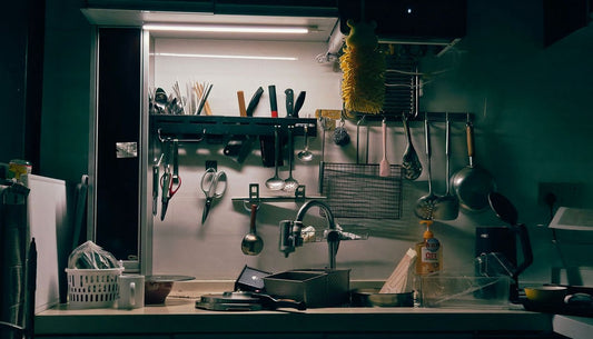 A small kitchen with utensils, knives and pans hanging on a rail above the counter.