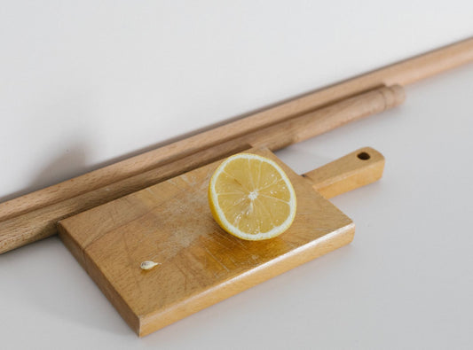A slice of lemon on a light wooden chopping board with a handle.
