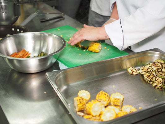 A cook prepping food at a stainless steel kitchen counter with steel bowls and trays.