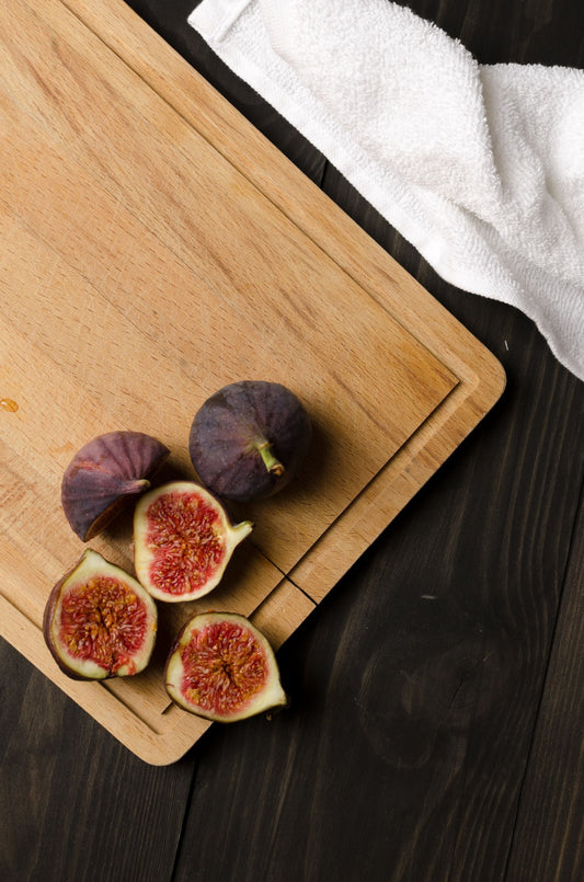 Halved figs on a large wooden cutting board on a dark table.