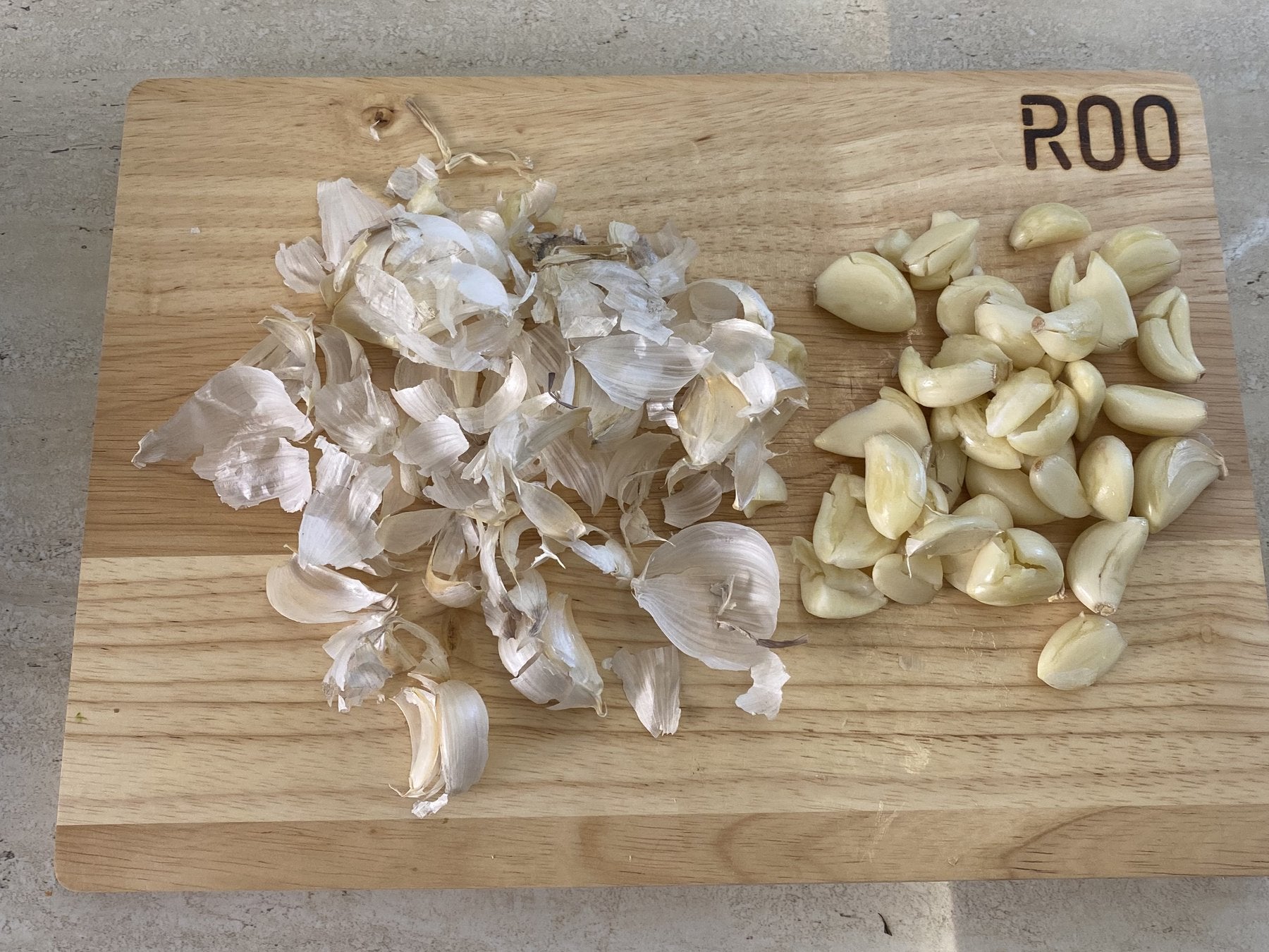Garlic skins covering half of a cutting board, with the peeled cloves squeezed onto the other half